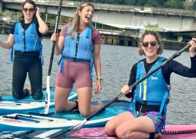 Friends laughing on paddleboards during a watersports hen do in Bristol